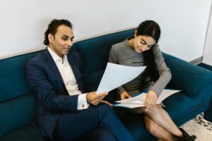 A man and woman in a professional setting discussing paperwork on a couch.